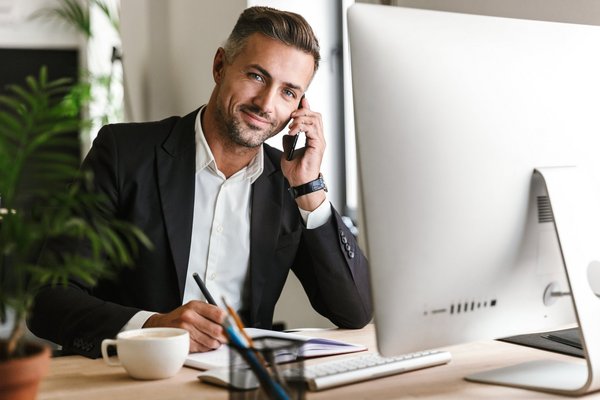 Mann am Schreibtisch während er vor dem Computer telefoniert